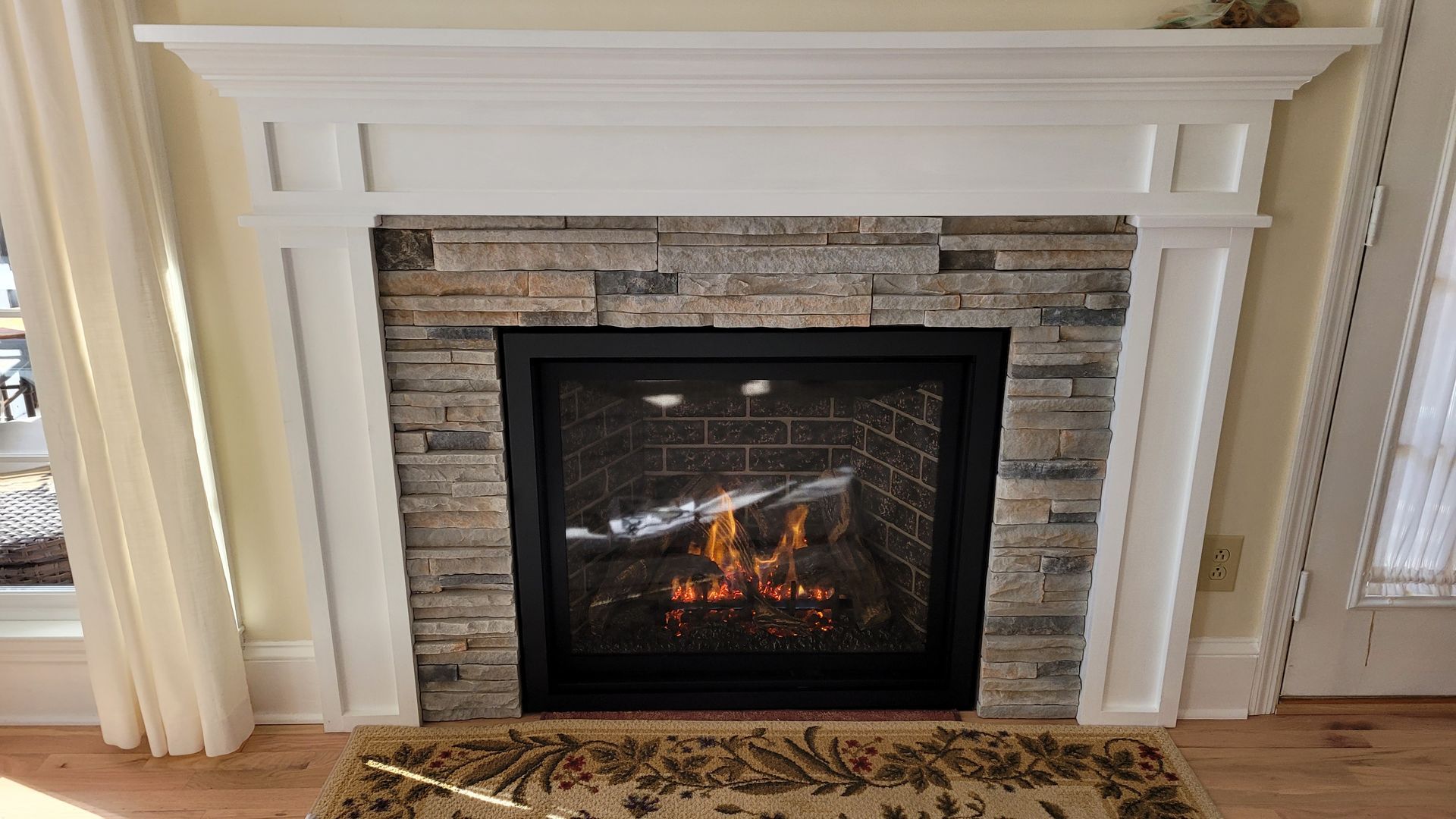 White fireplace mantel with stacked-stone surround and lit electric fire in a living room