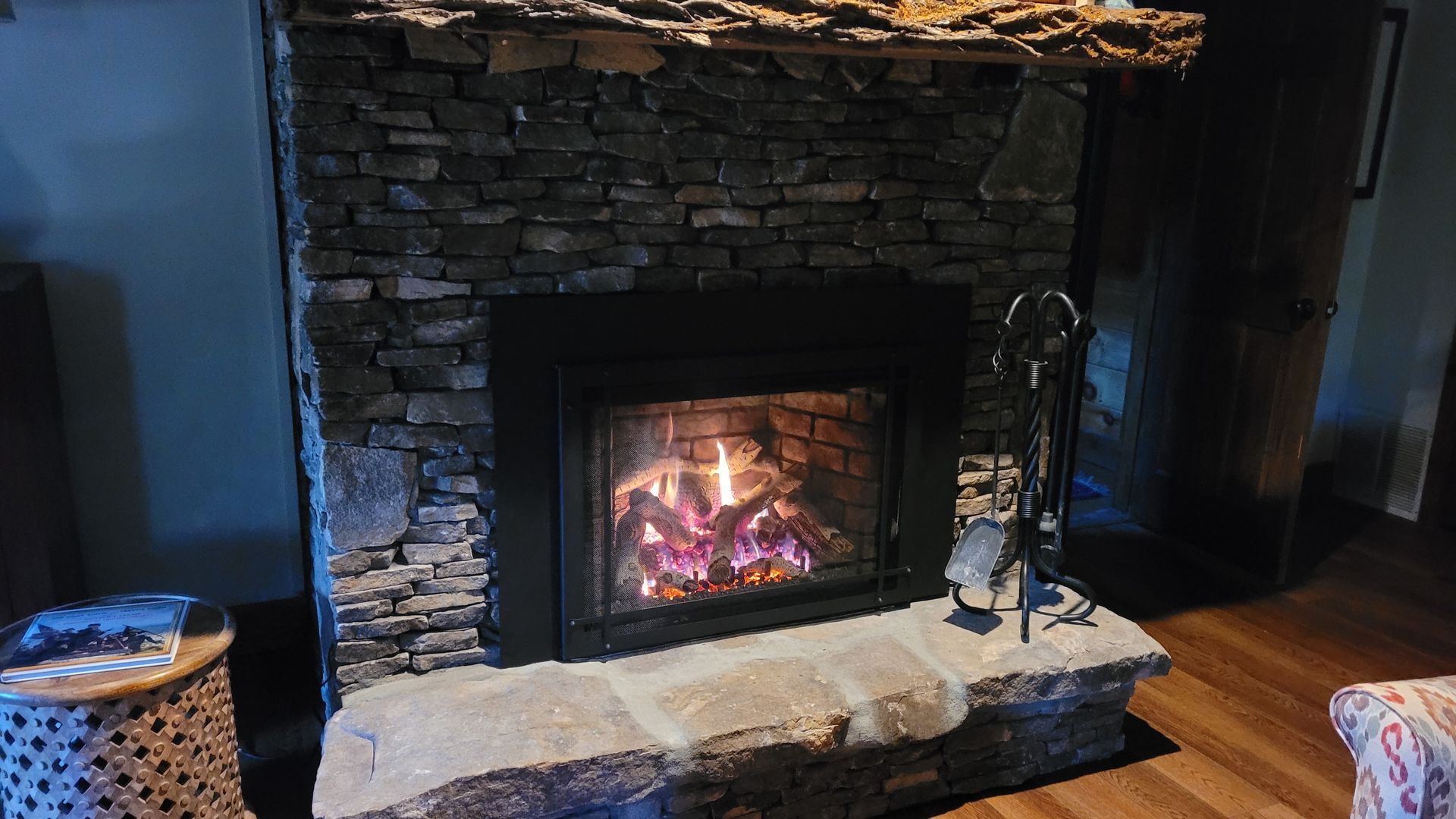 Stone fireplace with a lit fire, black surround, and decorative items on the hearth in a dim room