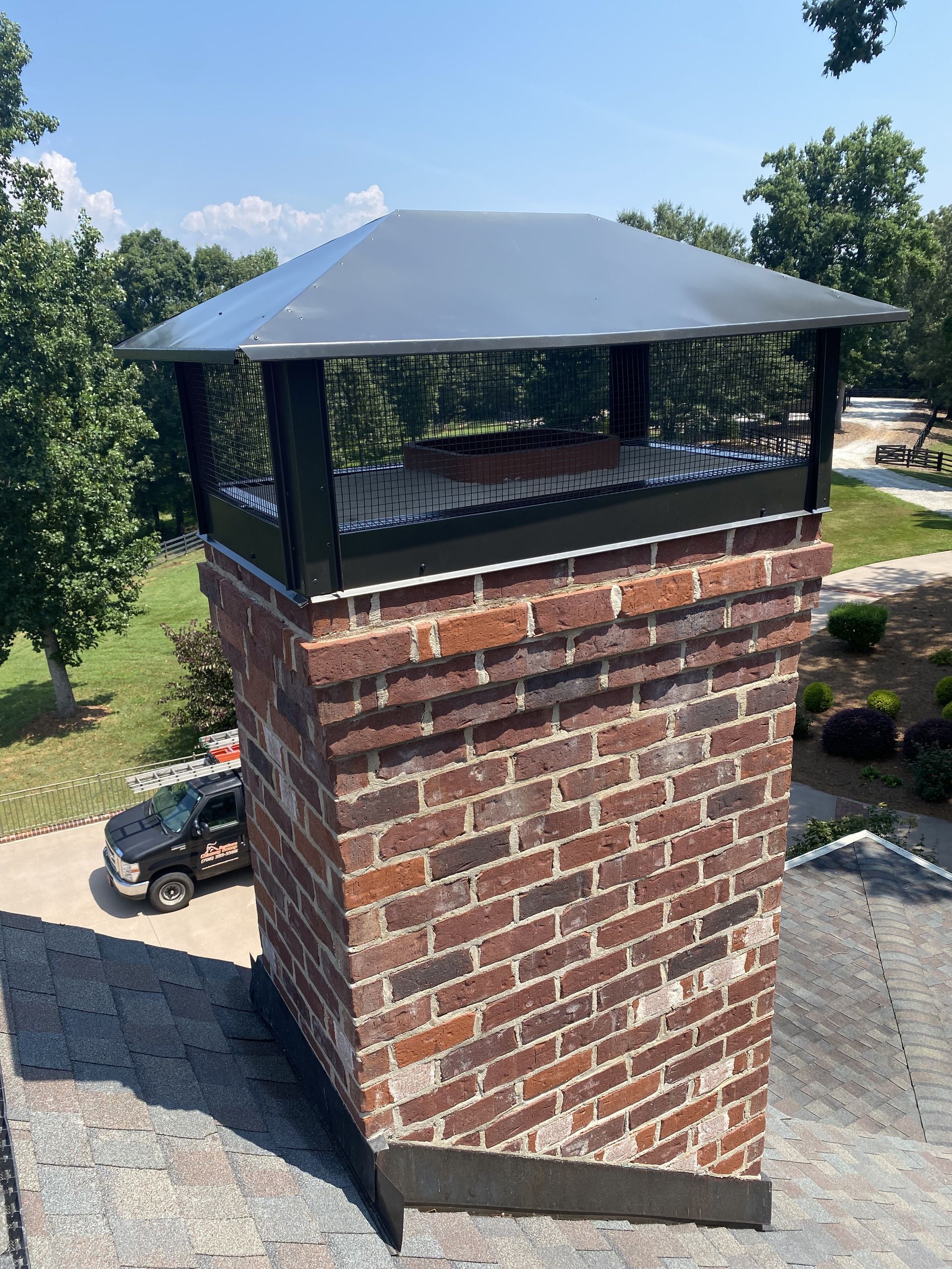 Brick chimney with black metal cap on a rooftop outdoors under a blue sky
