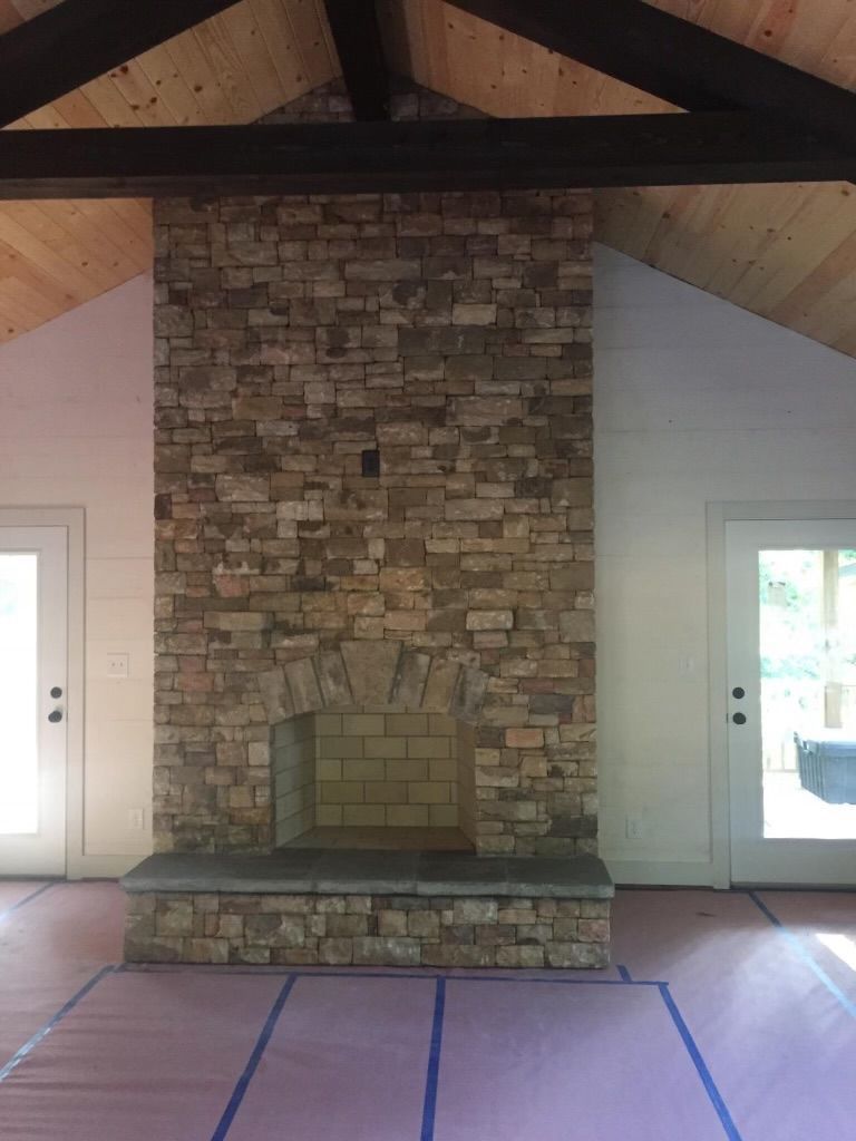 Stone fireplace centered in a room with white walls, exposed beams, and doors on both sides.