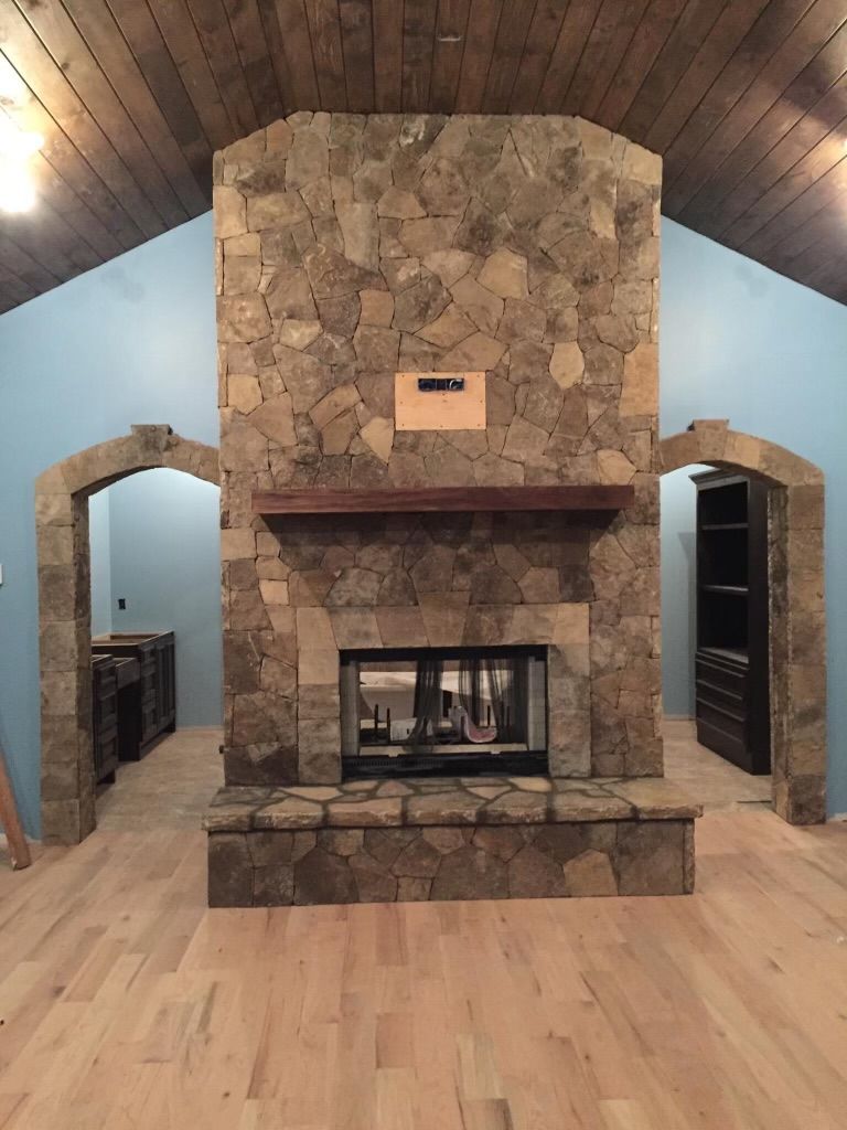 Stone fireplace centered in a rustic room with wood ceiling, light walls, and hardwood floor