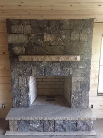 Stone fireplace with raised hearth and wooden mantel in an unfinished room