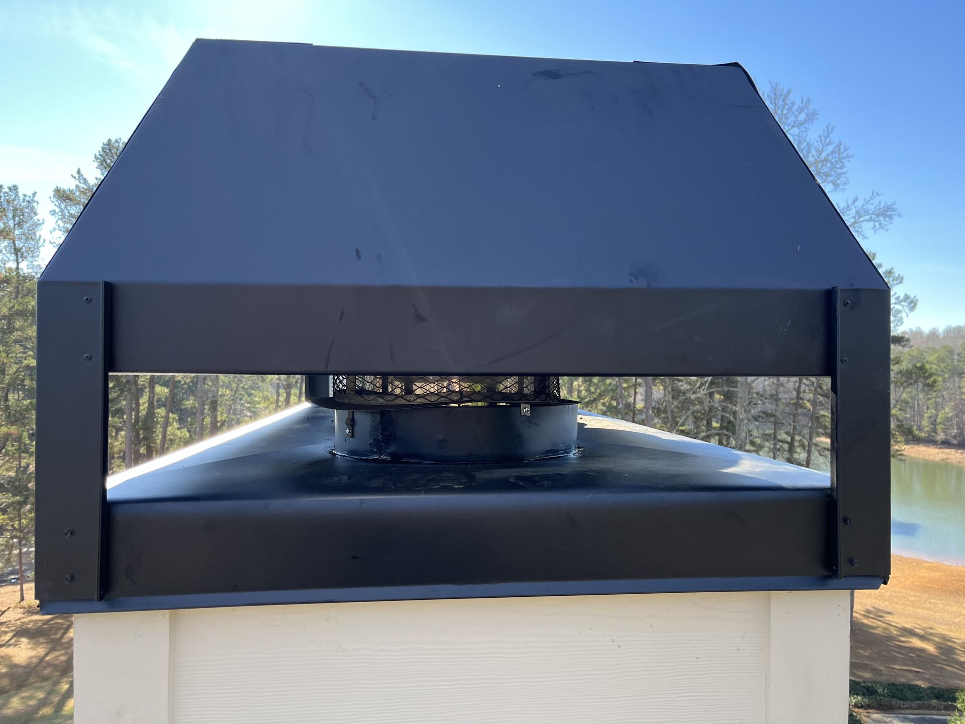 Black metal rooftop vent or exhaust cap on a white structure against a blue sky