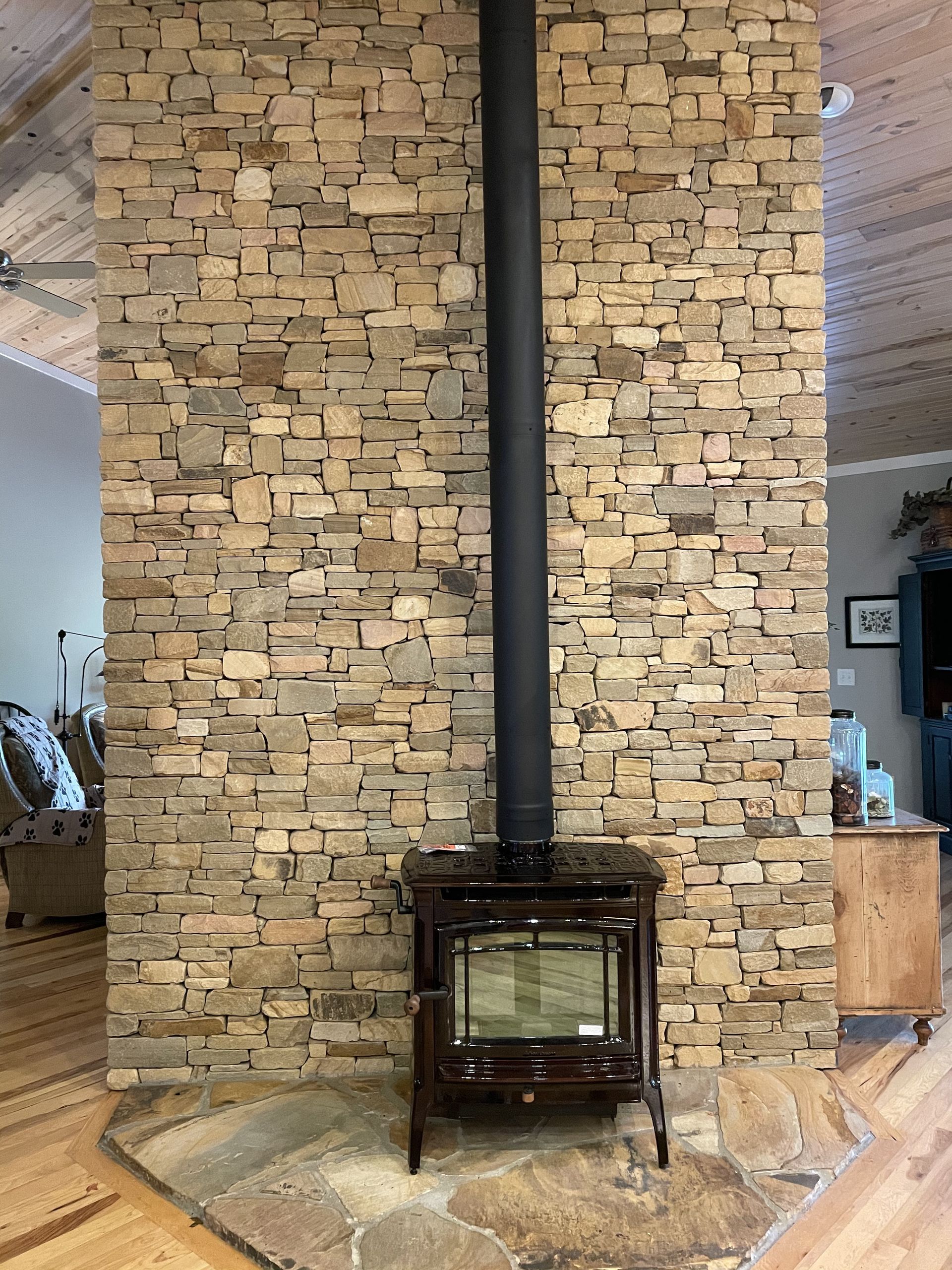 Stone fireplace wall with a black wood stove and chimney in a rustic interior