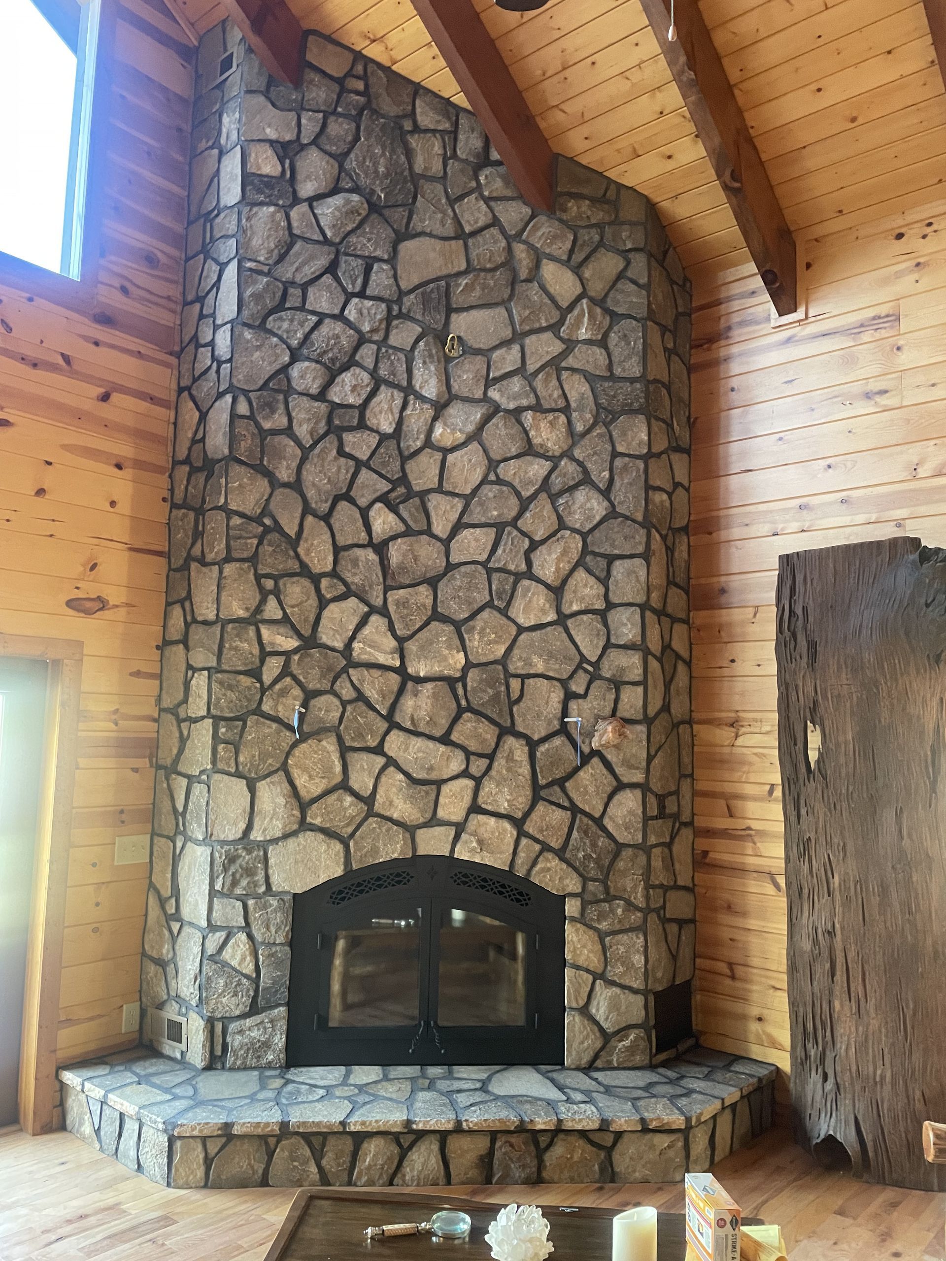 Stone fireplace in a wood-paneled room with vaulted ceiling and windows