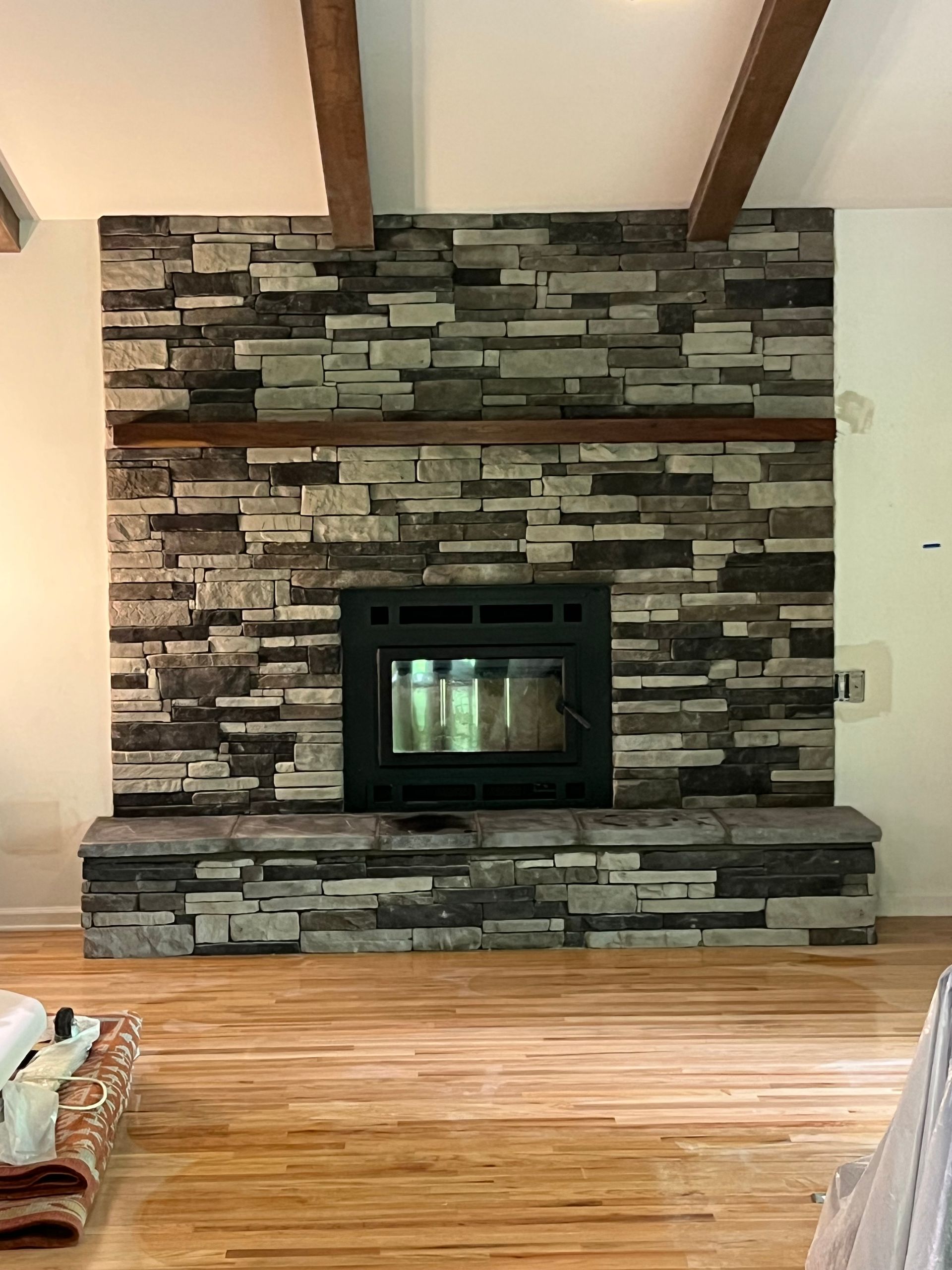 Stone fireplace with a black insert in a room with hardwood floors and exposed ceiling beams