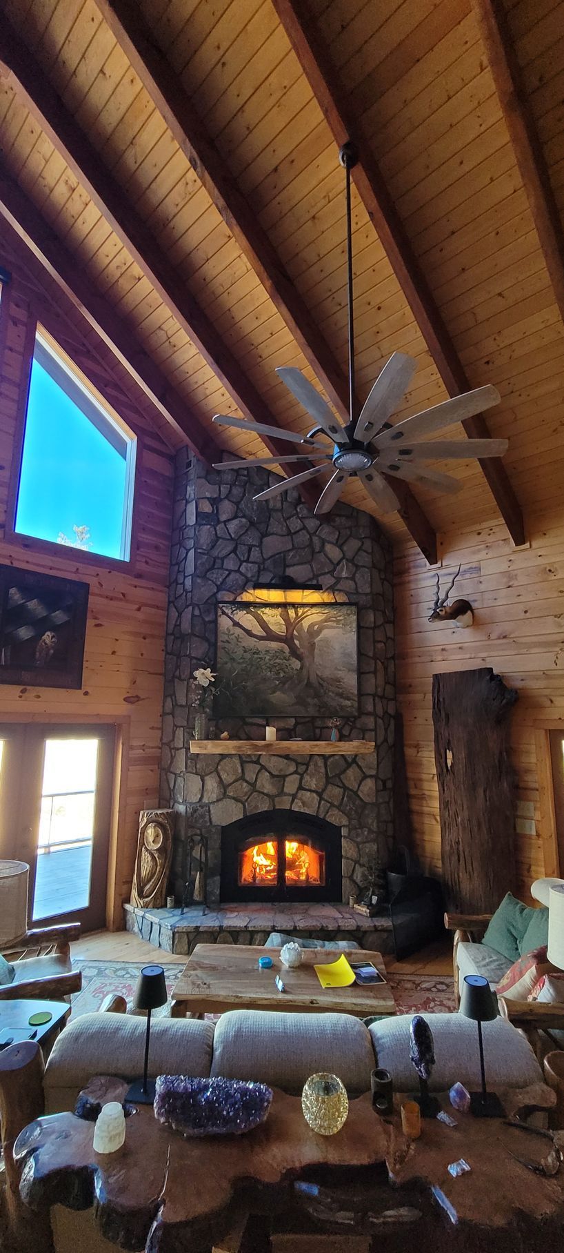 Rustic lodge living room with stone fireplace, wood beams, and a large wagon-wheel chandelier