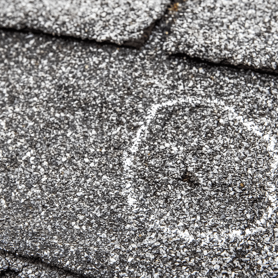 Close-up of dark gray asphalt shingles with a circular patch in the center