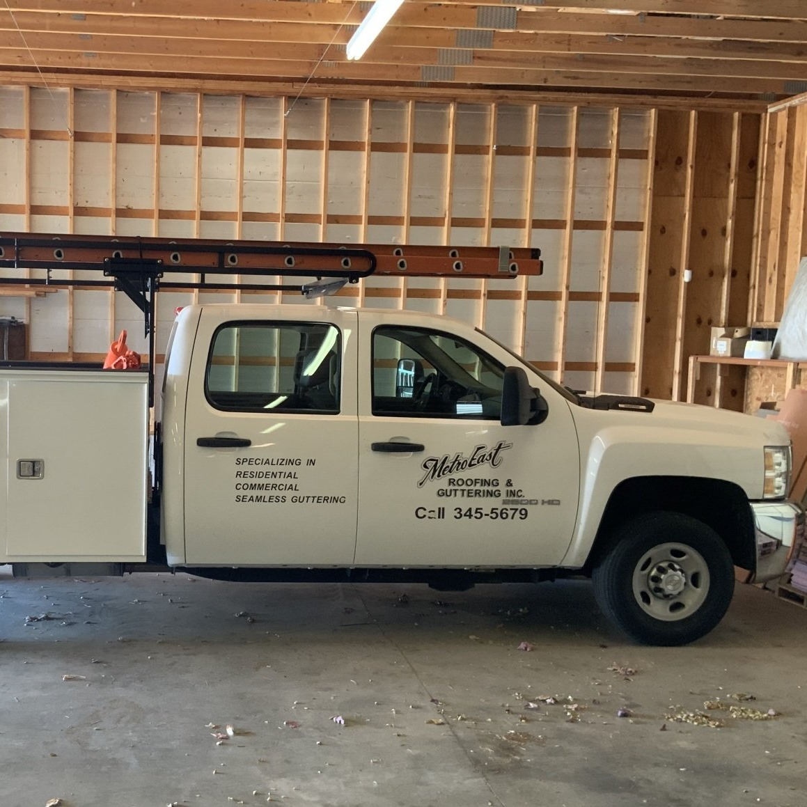 White utility pickup truck with ladder rack parked inside an unfinished wooden garage.