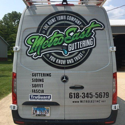 Van with Metro East Gutters logo, services list, phone number, and license plate on the back on a street.