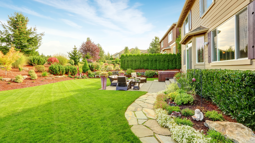 Landscaped backyard with green lawn, stone path, patio seating, and a house exterior