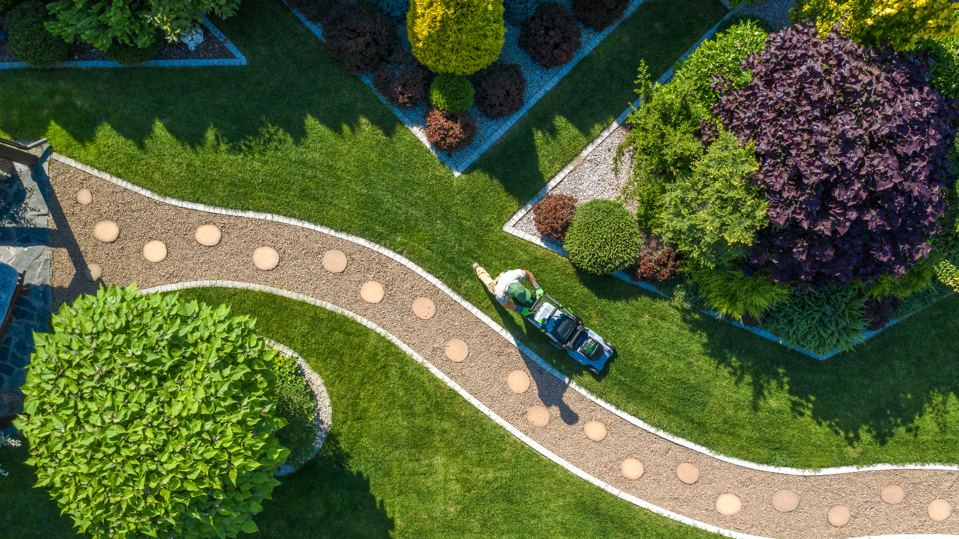 Overhead view of a curving garden path with a person and bicycle beside green lawns and purple flowering trees