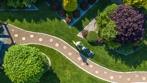 Aerial view of a landscaped garden with winding stone path, green shrubs, and a purple tree