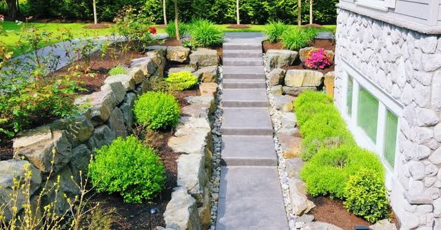 Stone garden path with steps between landscaped rocks and green shrubs beside a white house