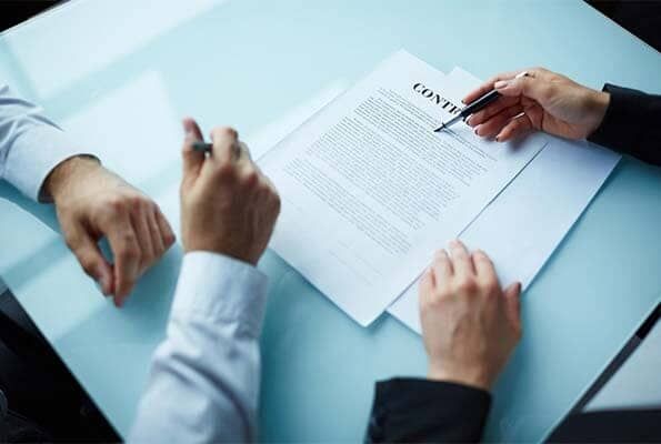 Dos personas están sentadas en una mesa firmando un contrato.