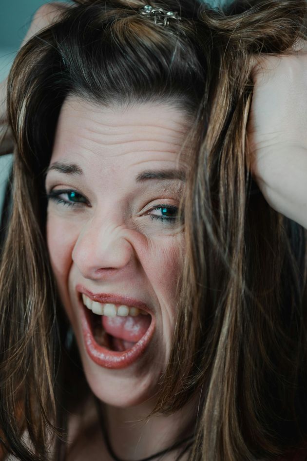 A close-up of a person with long brown hair, scrunching their face in frustration with their mouth open.