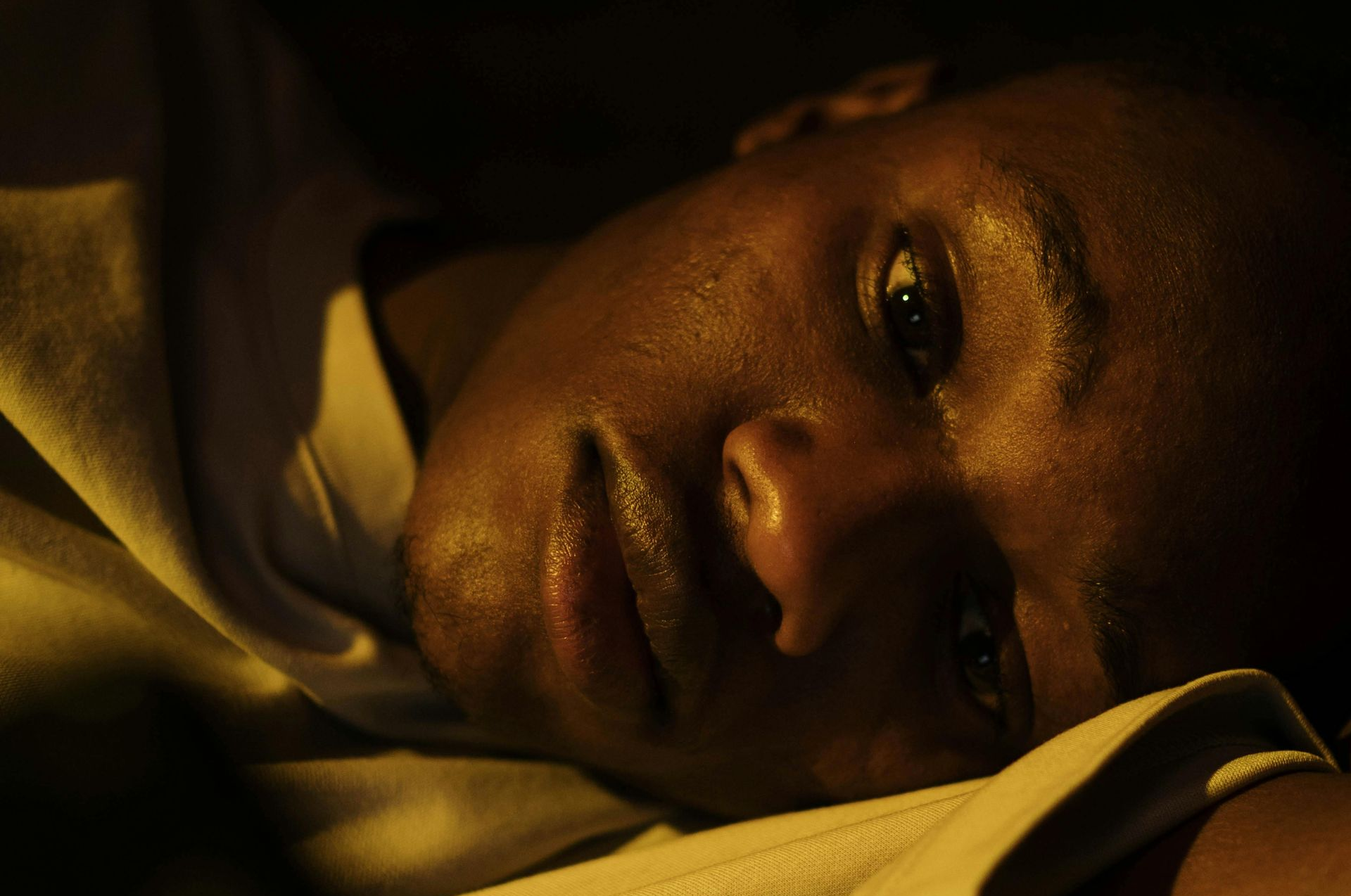 A person's hand with fingers spread, covering their face, rendered in a warm, soft-focus, golden-yellow light.