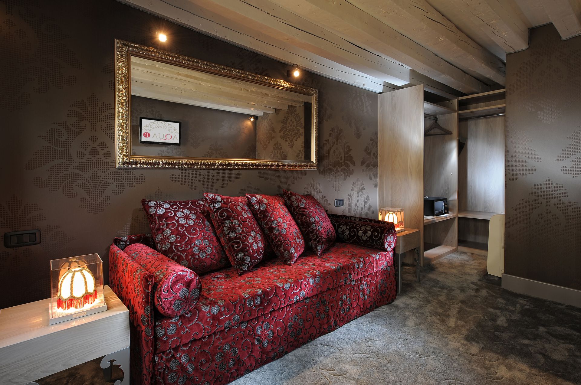 Cozy living room with a red patterned sofa, large mirror, and warm lighting under exposed beams