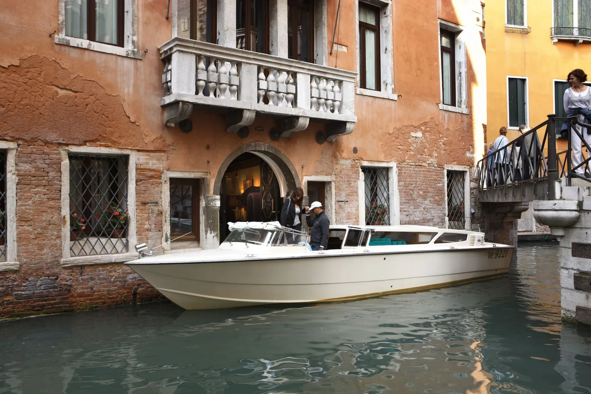 White motorboat on a canal beside an orange building with a balcony and stone steps