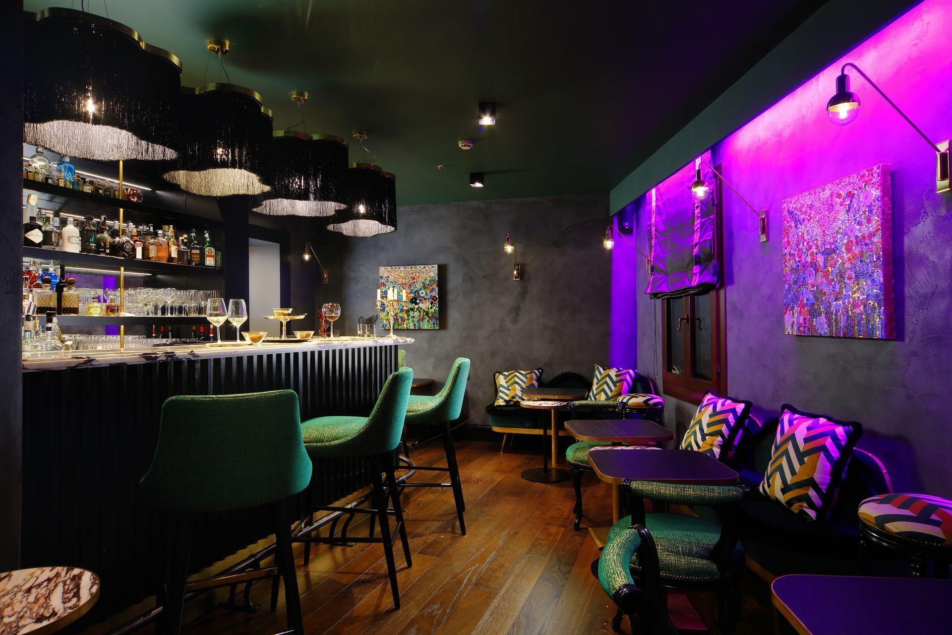 Bar elegante con iluminación tenue, sillas verdes, iluminación ambiental en color púrpura y una pequeña zona de estar.