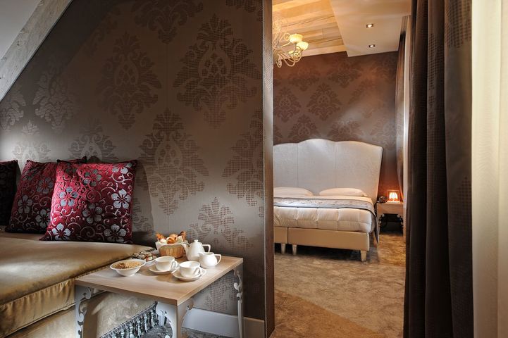 Elegant hotel suite with patterned walls, plush seating, and a bed in the adjoining room