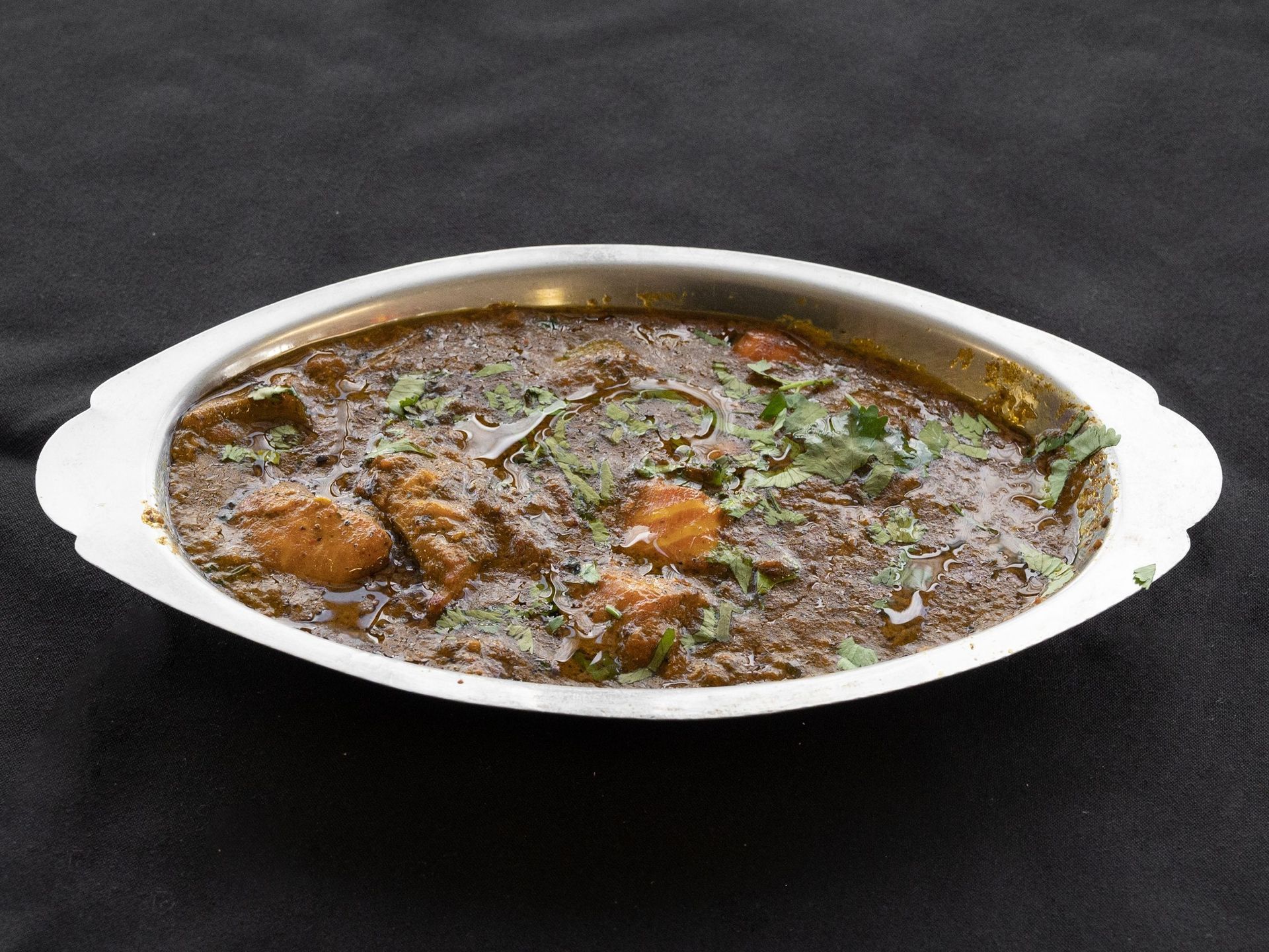 Chicken curry in a silver serving dish, garnished with fresh cilantro on a dark background.