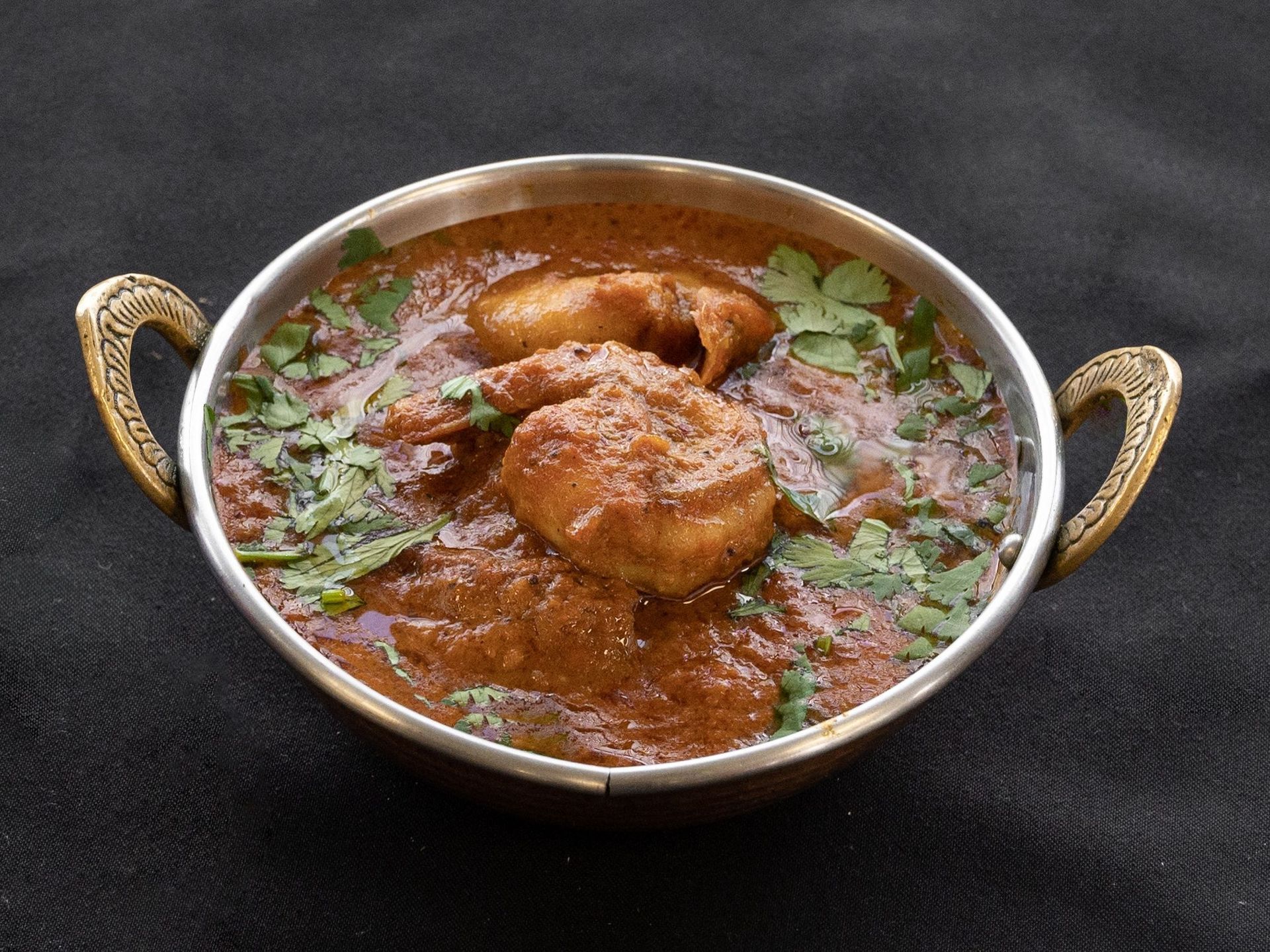 Chicken curry in a bronze bowl, garnished with cilantro, on a black surface.