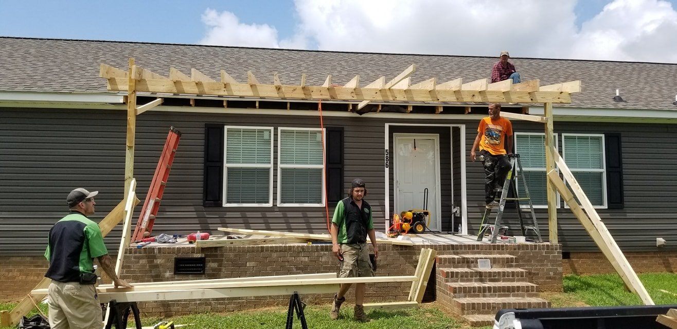 Workers building a porch awning on a house. Men work on the wooden frame, using ladders, and hand tools.