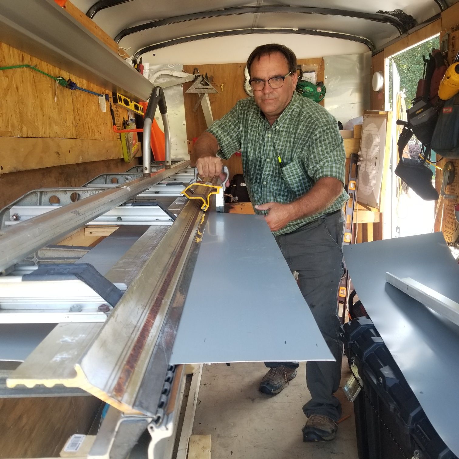 Man using a sheet metal bender in a trailer, wearing a green shirt and brown pants.