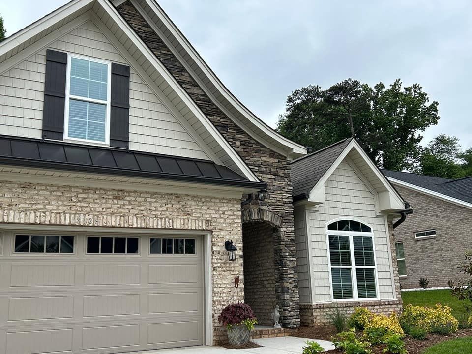 Beige brick and tan garage door house with black roof, shutters, and stone archway.