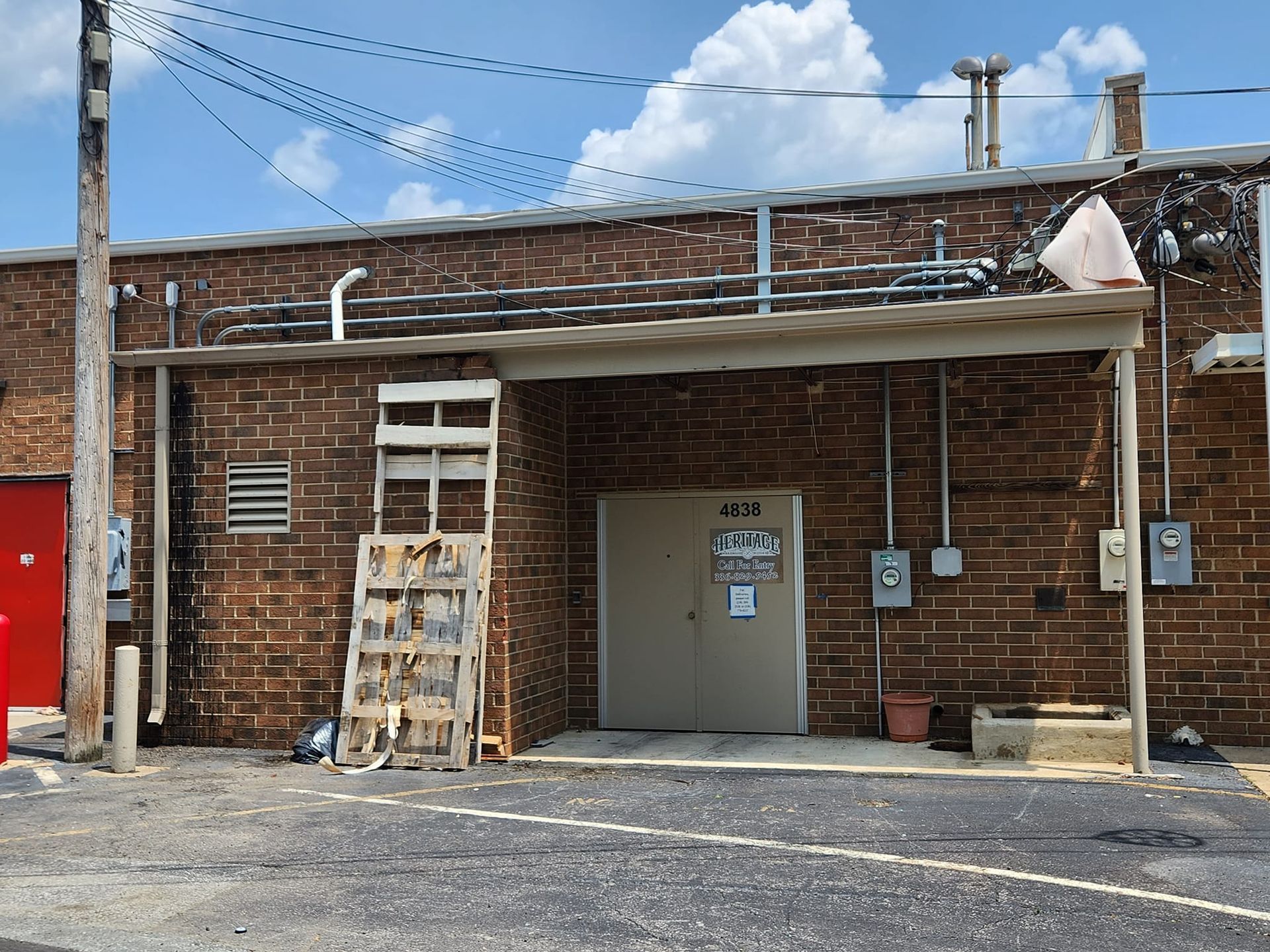 Brick building with an entrance under a metal overhang. A wooden ladder leans against the wall.