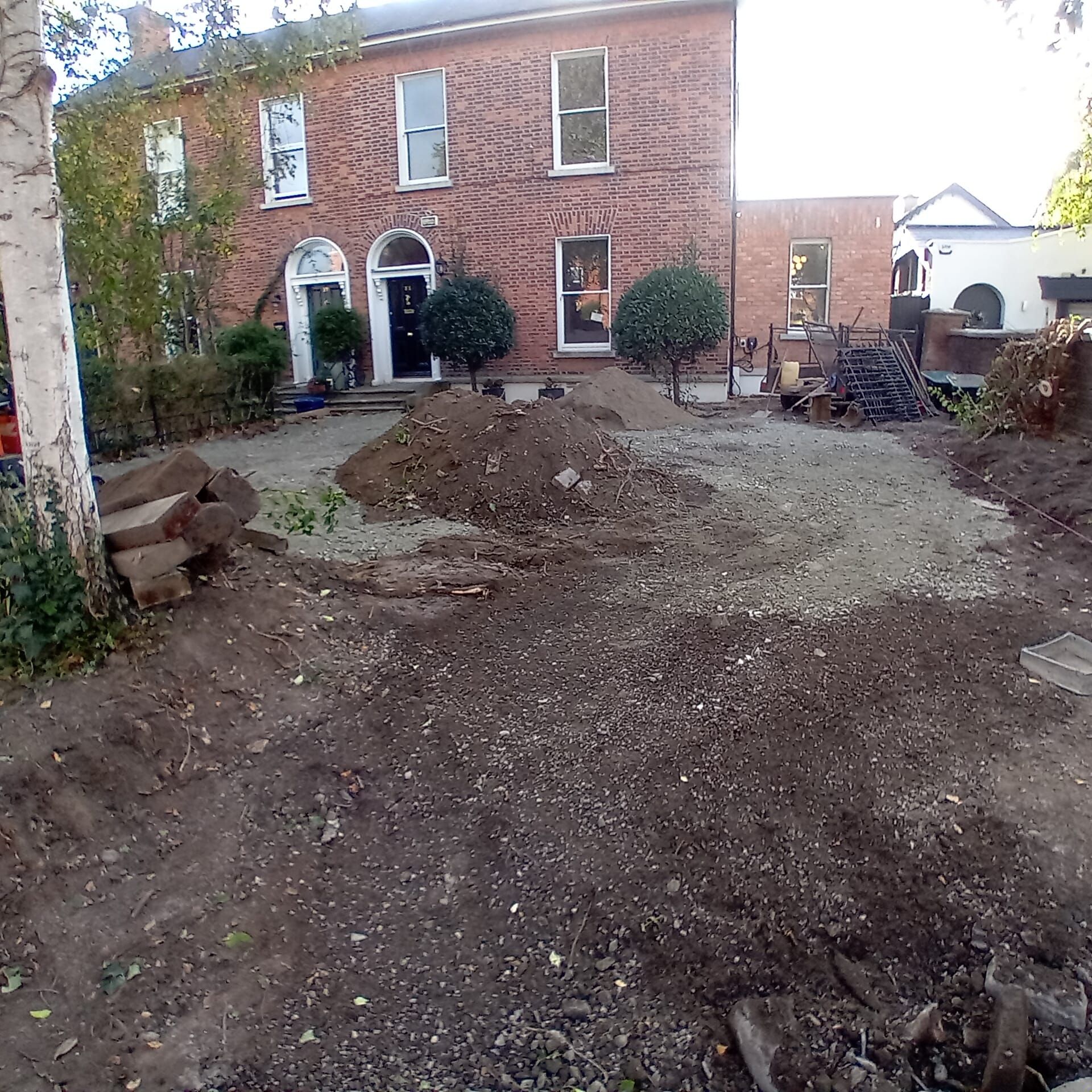 A house under renovation with a cleared front yard. Brown dirt, gravel and a pile in front of the brick building.