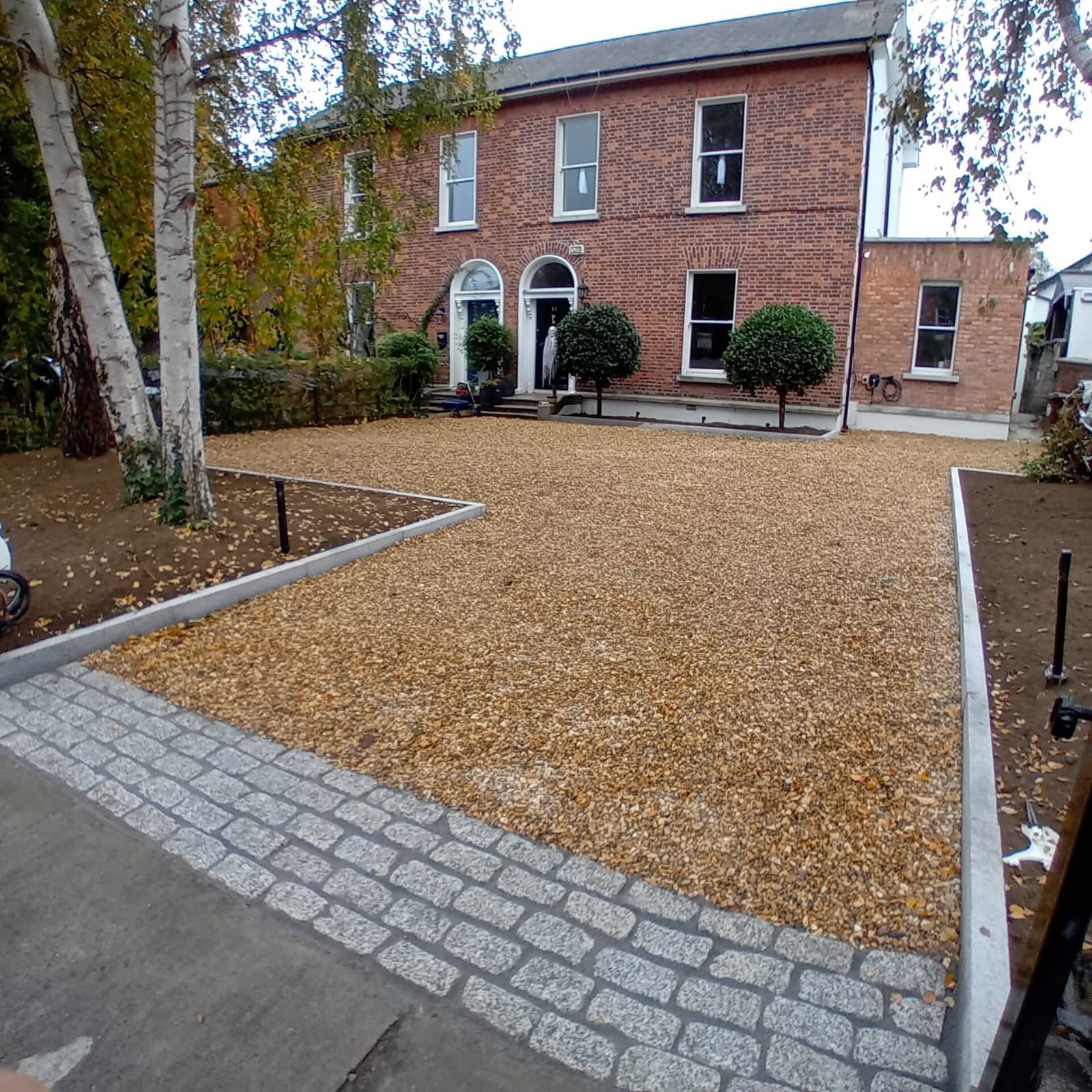 A gravel driveway in front of a brick building with a granite stone border.