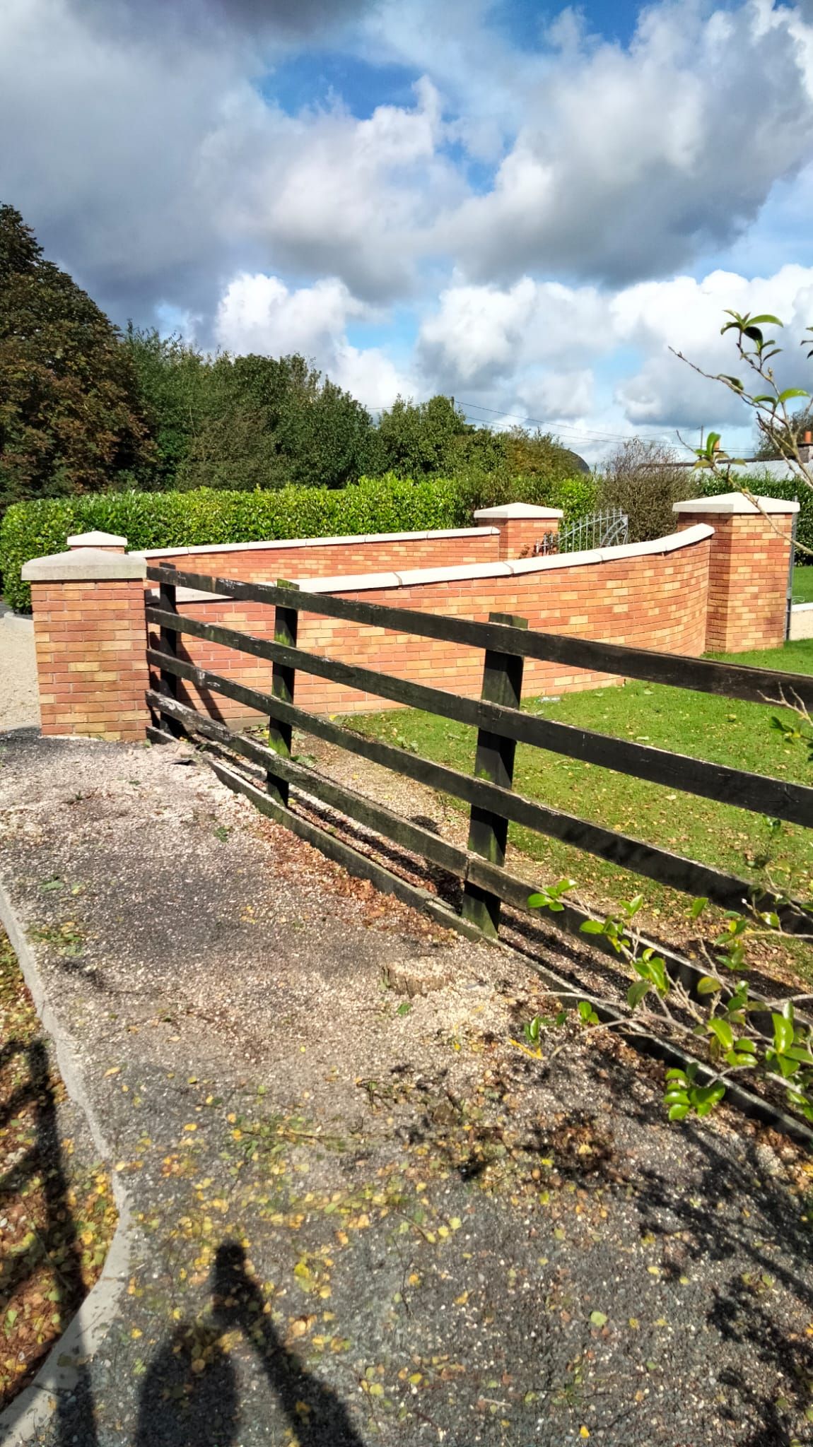 Brick wall with wooden fence, under cloudy sky, green grass.