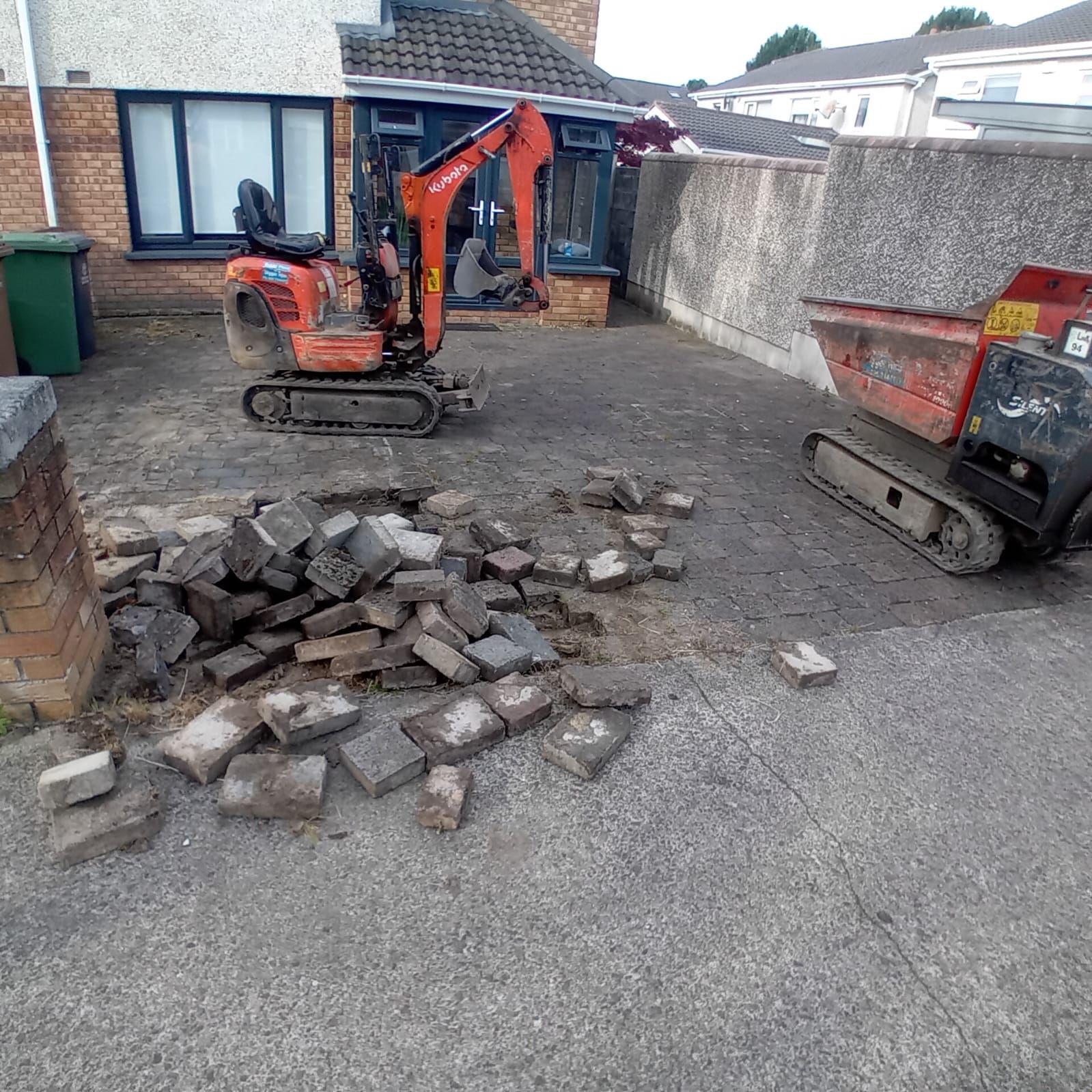 A house under renovation with a cleared front yard. Brown dirt, gravel and a pile in front of the brick building.