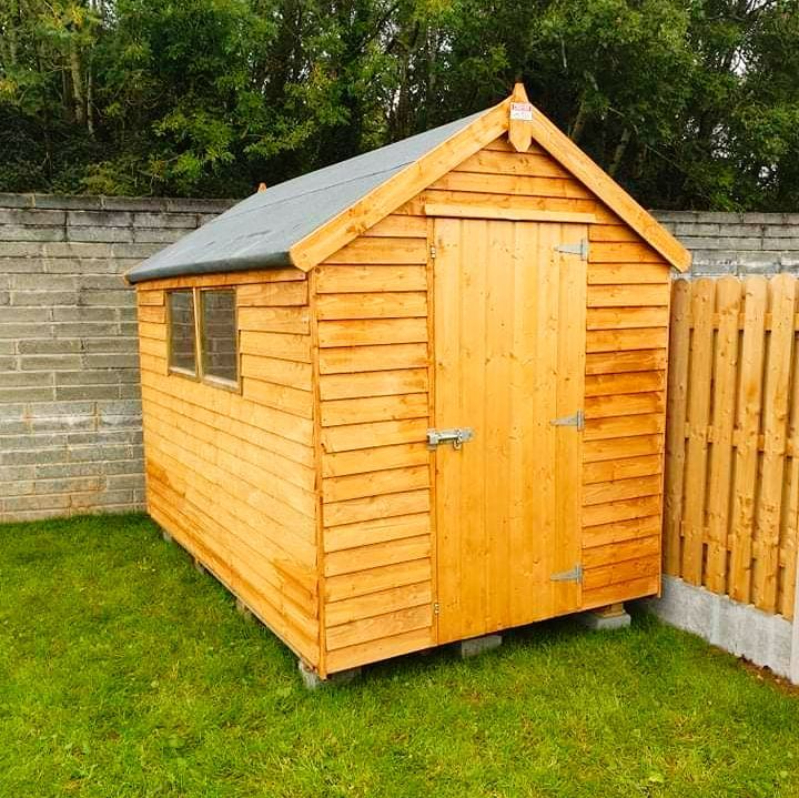 Wooden garden shed with door and small window, set on grass between walls and a fence.