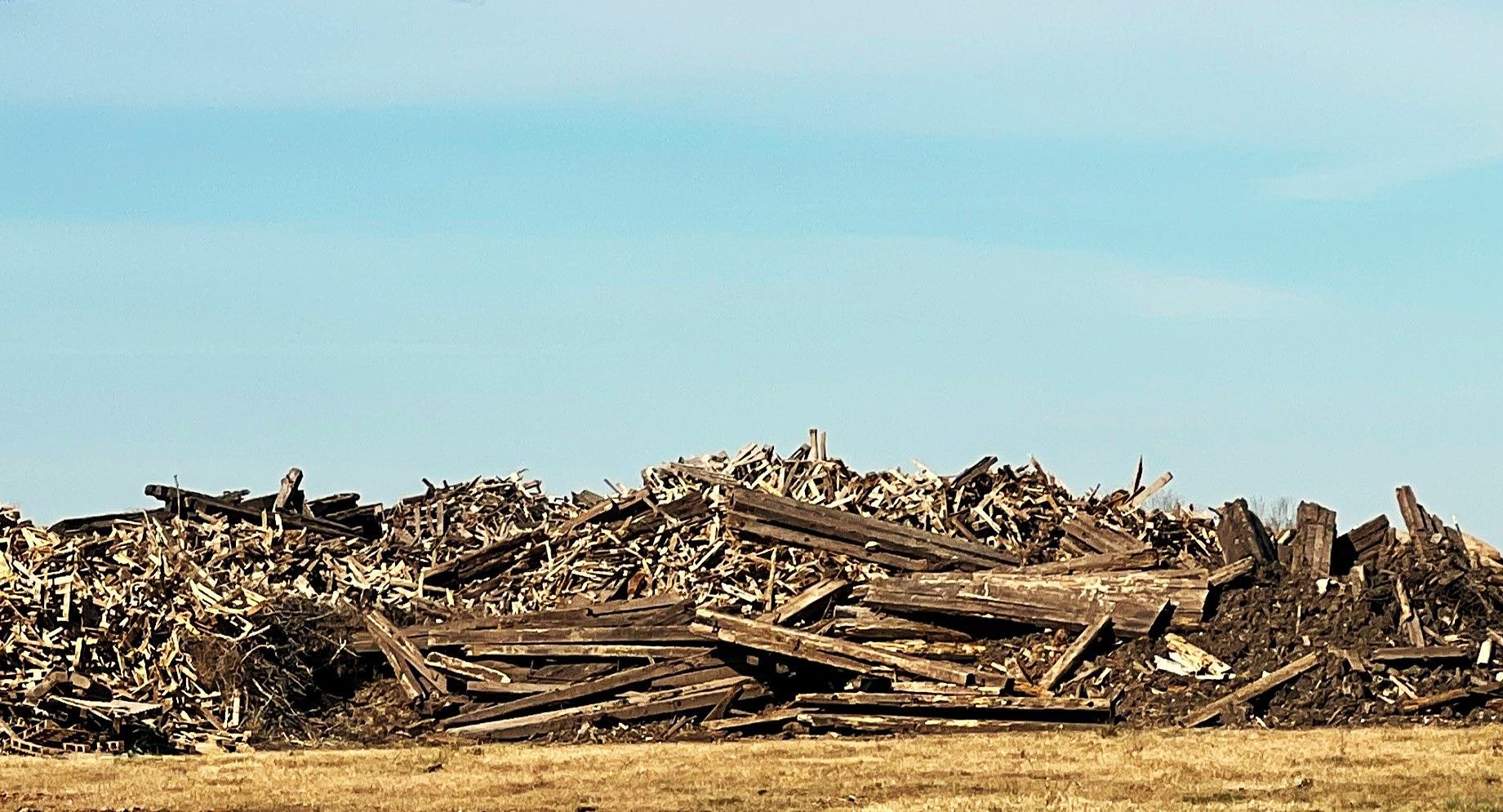 Pile of weathered wood scraps against a blue sky, on a brown field.