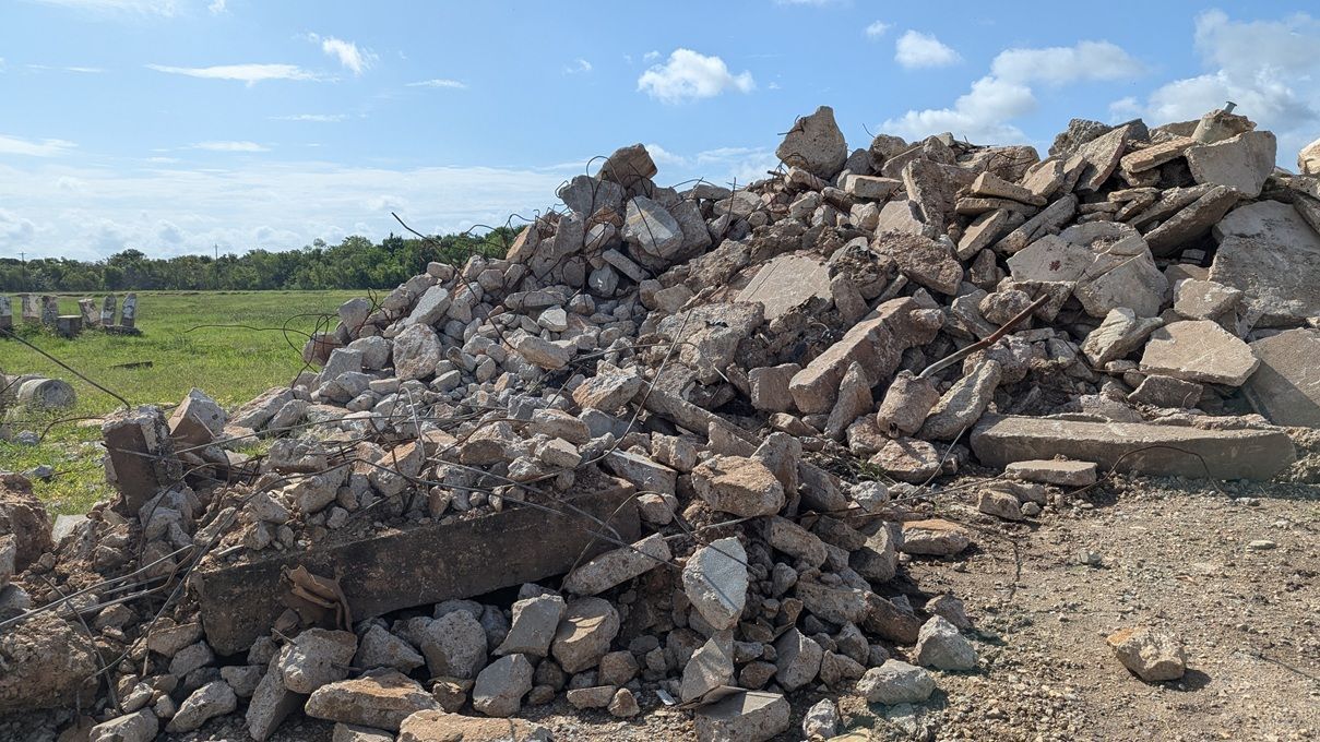 Pile of broken concrete debris with green field and blue sky in the background.