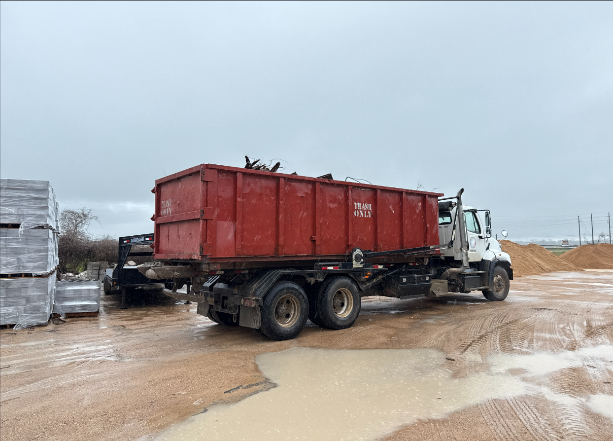 Red dumpster on a white truck in a muddy outdoor area.