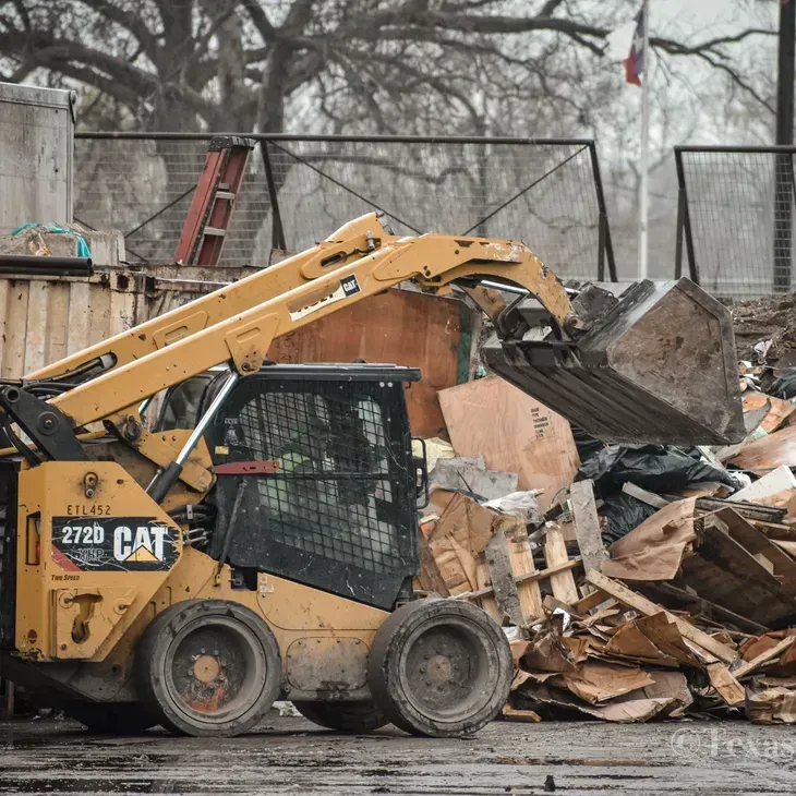 Yellow Caterpillar skid steer loader with raised bucket moving debris.