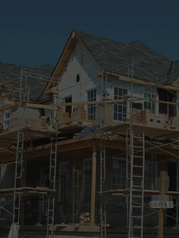 House under construction, scaffolding surrounding the structure, dark sky overhead.