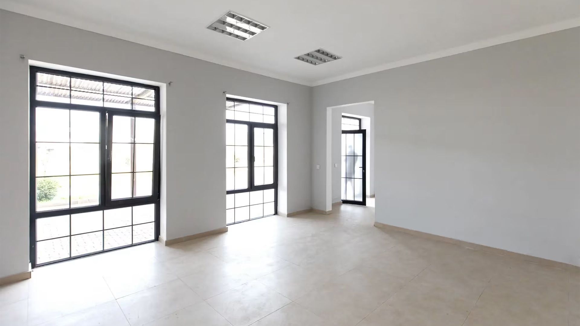 Bright empty room with large windows, light wood floor, and gray walls