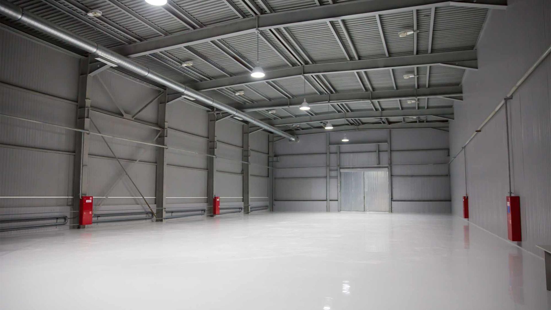 Empty industrial warehouse with white floor, gray walls, and red safety equipment along the sides