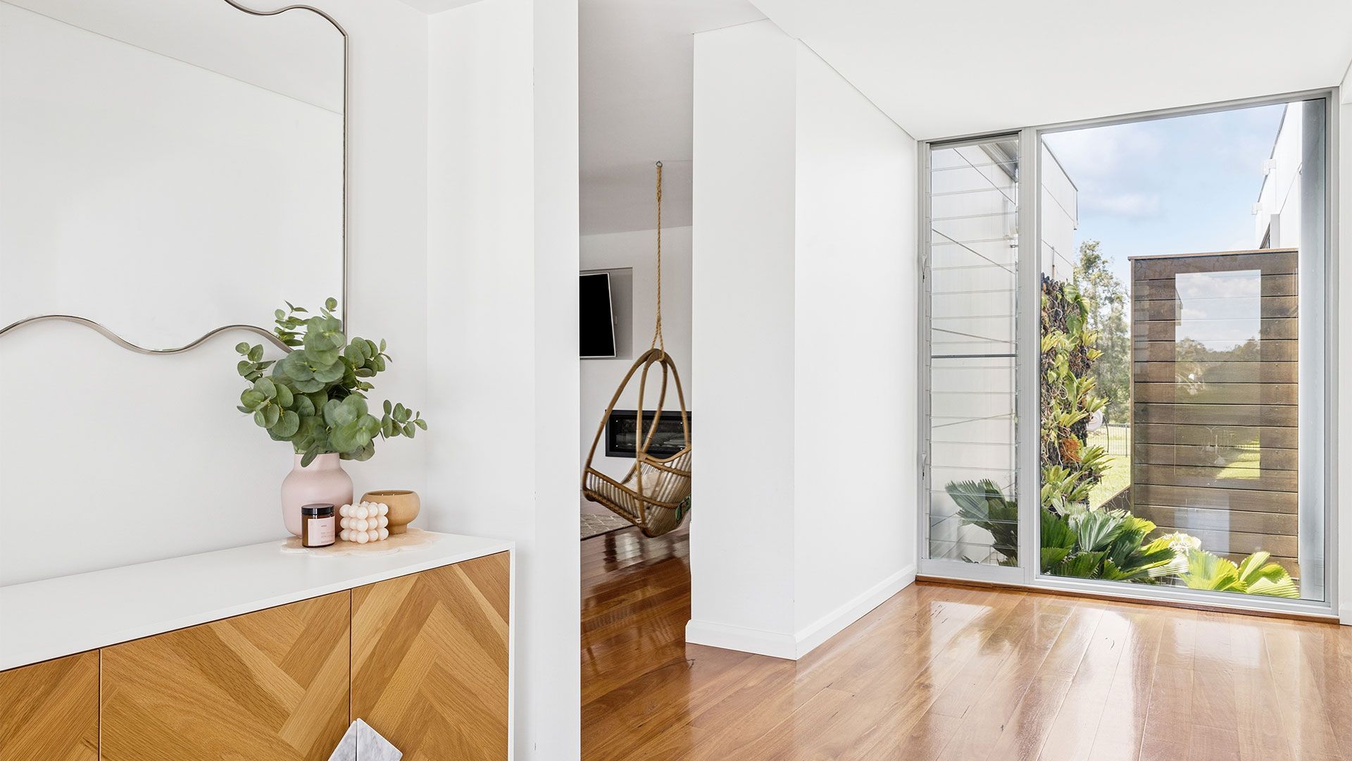 Bright, empty modern room with wood floors, white walls, ceiling fan, and tall windows.