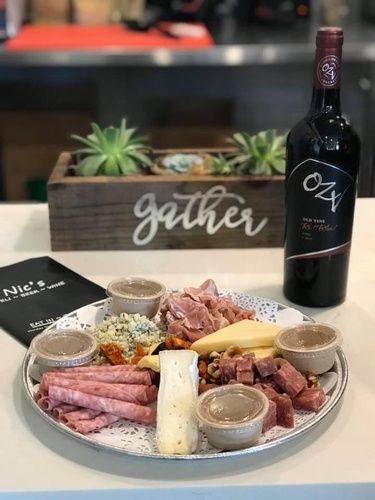 Charcuterie board with meats, cheese, crackers and dips beside a bottle of red wine on a table