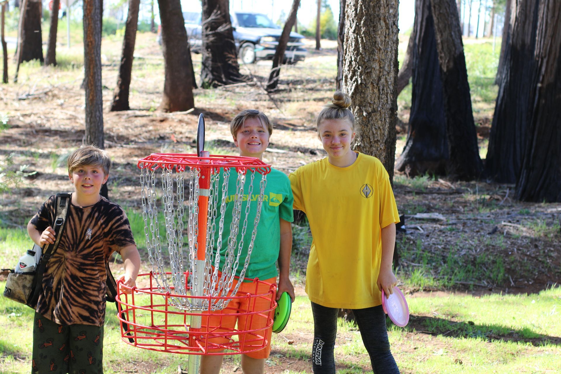 Three young boys are standing next to a frisbee golf basket in a park in Paradise and Magalia, California.