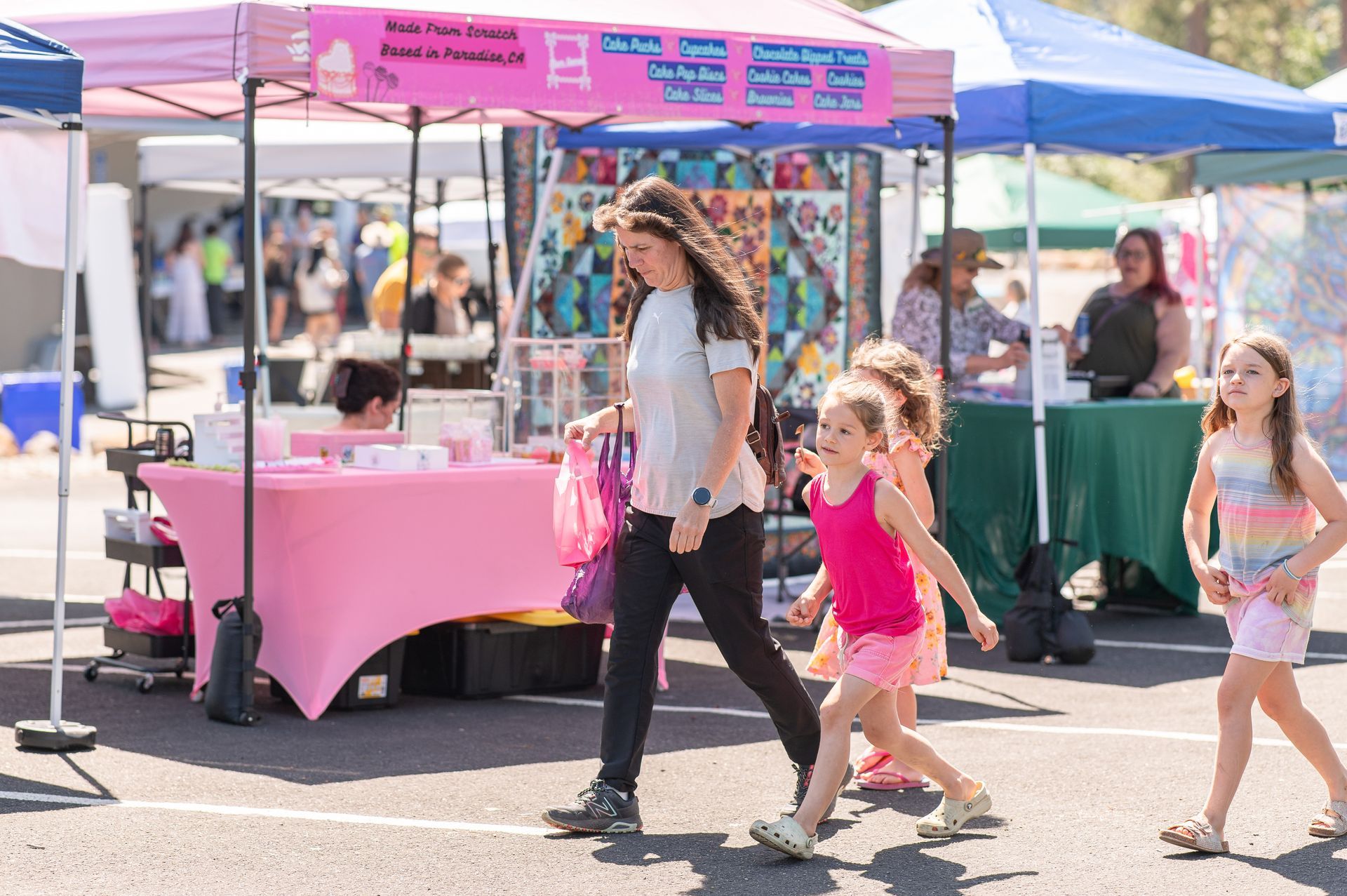 People walking past a pink market stall at an outdoor fair.