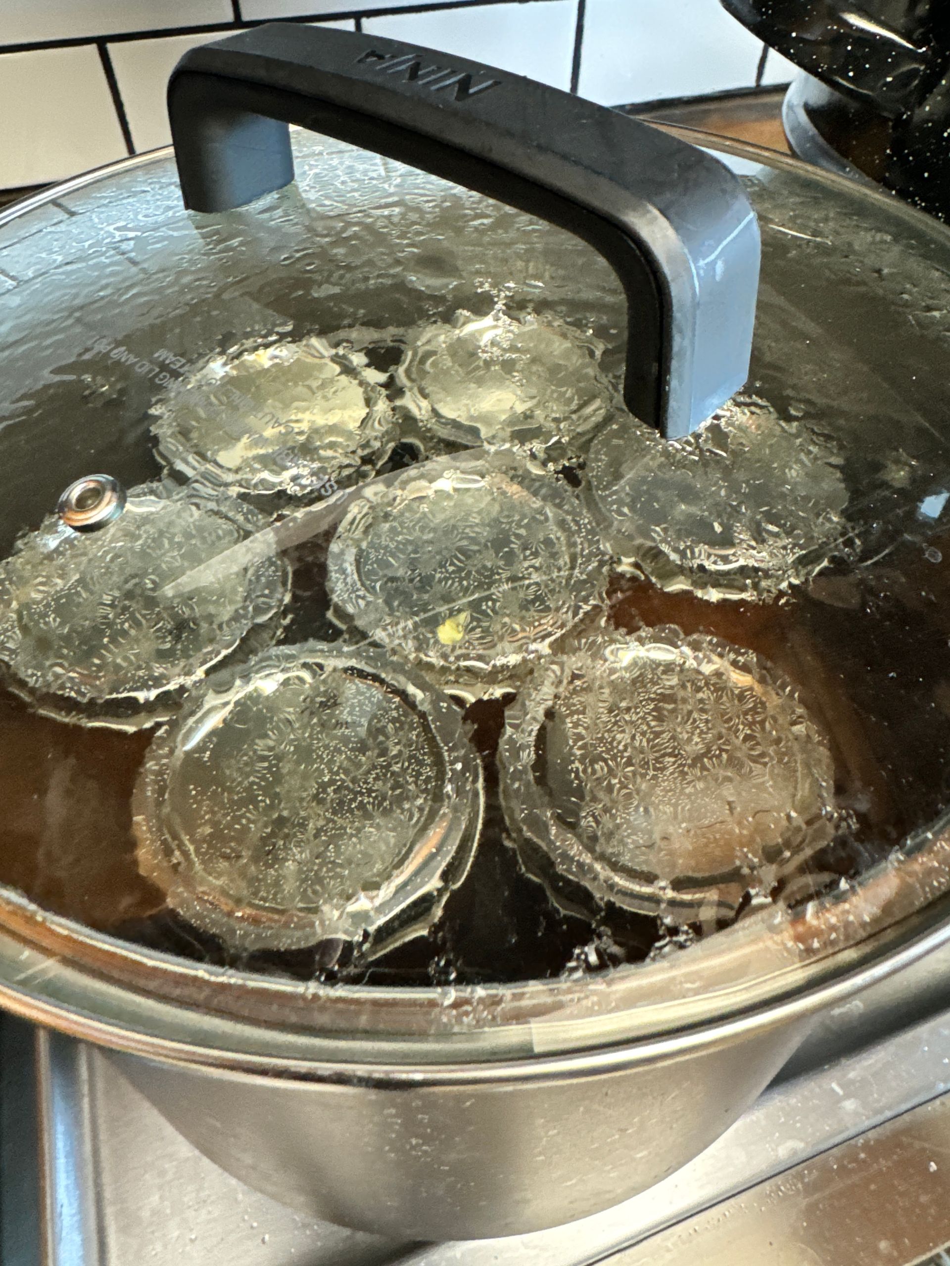 Pot of water with several glass jars boiling under a black lid handle