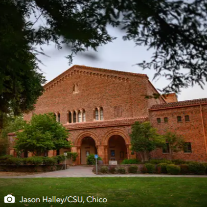 Brick campus building with arched entrance and trees framing the front lawn