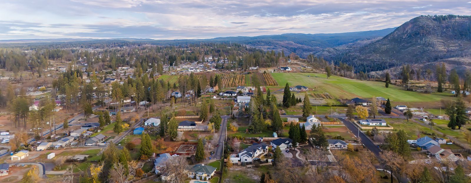 Aerial view ofParadise California with houses, green fields, and a mountain under a cloudy sky.